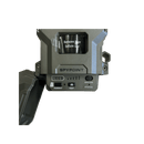 A SpyPoint Flex-M2 electronic device in dark gray and black, featuring a hinged side panel, a central window with a tape roll, and front buttons labeled Format, Test, and Status.